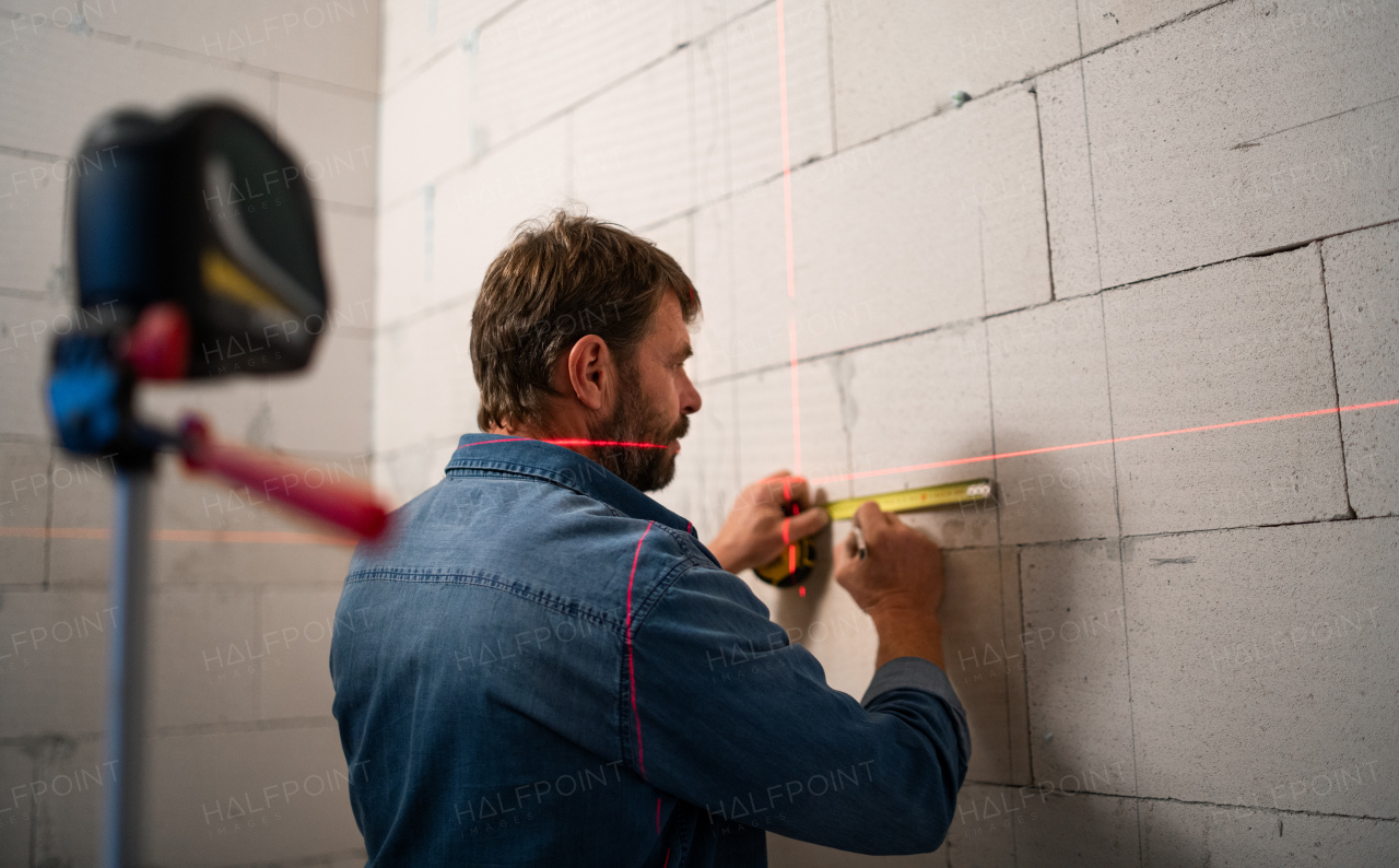 A handyman working on construction site, measuring wall.