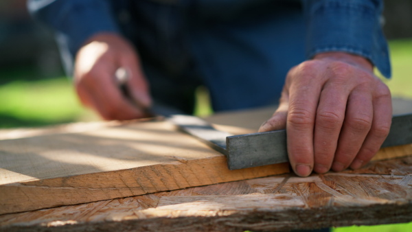 A close-up of handyman measuring a board, outside in garden.