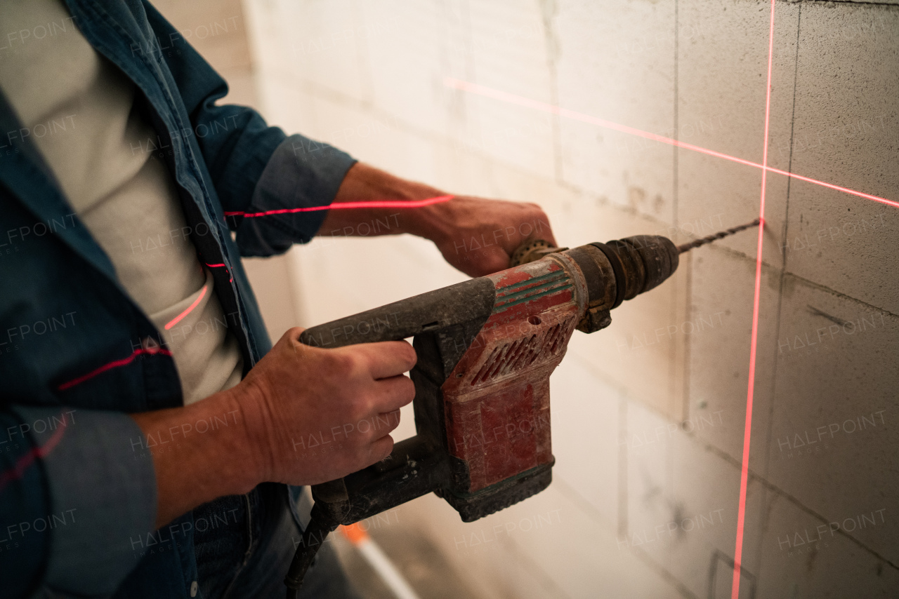 A close-up of handyman making a hole with drill on wall with help of laser leveler