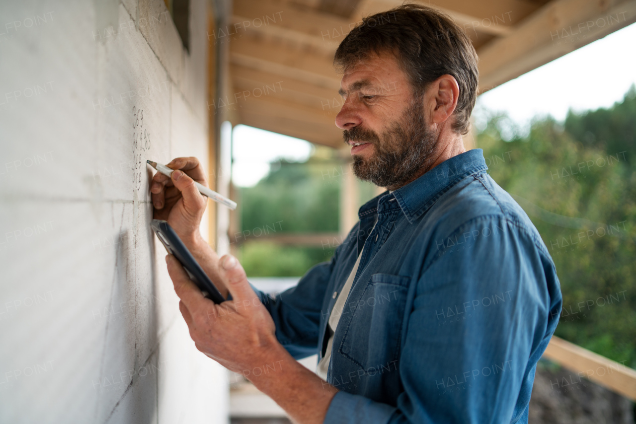 A handyman working on construction site, measuring wall.