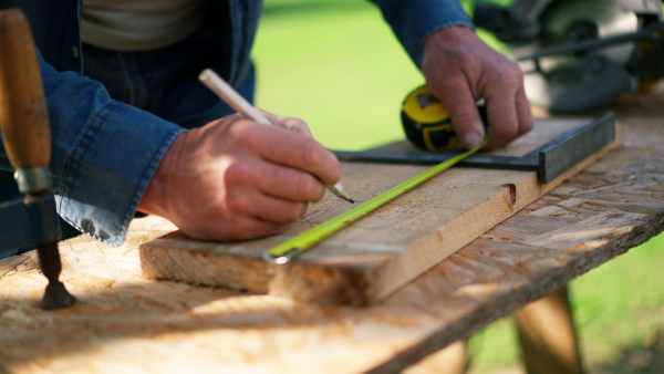 A close-up of handyman measuring a board, outside in garden.