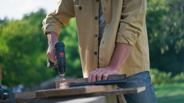 An unrecognizable handyman carpenter working in carpentry diy workshop outdoors with drill.