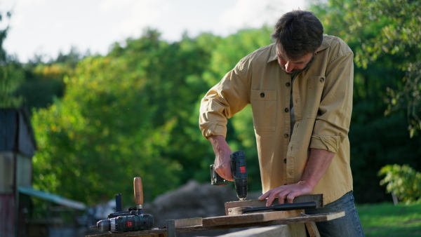 A handyman carpenter working in carpentry diy workshop outdoors with drill.