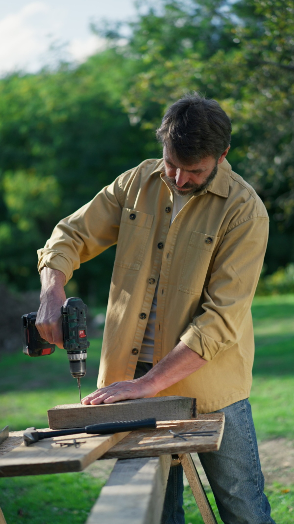 A handyman carpenter working in carpentry diy workshop outdoors with drill.