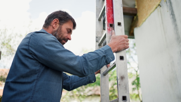 A high angle view of mature man climbing up the ladder