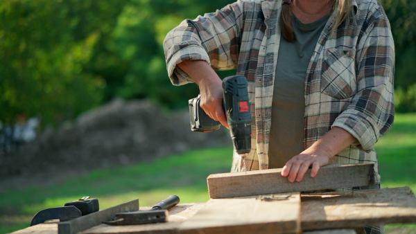 A happy handy female carpenter working in carpentry diy workshop outdoors with drill.