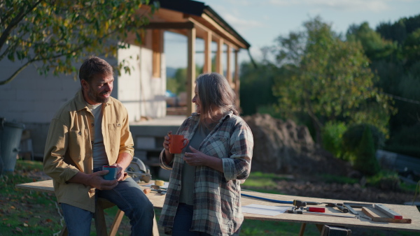 A mature couple having coffee break when working together on construction site of their new house.