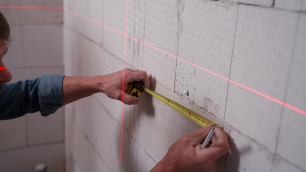 A handyman drawing a line on dry wall with help of laser leveler