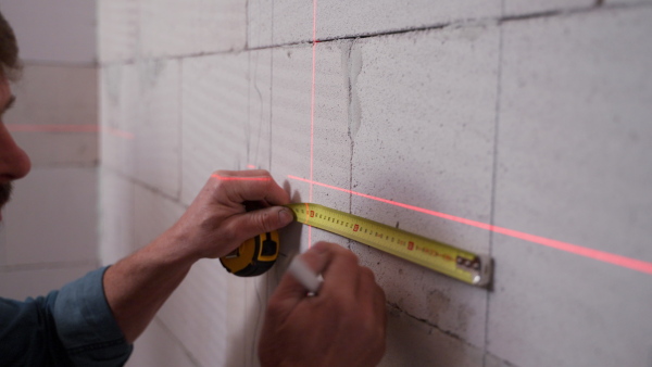 A handyman drawing a line on dry wall with help of laser leveler