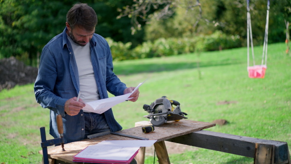 A mature man engineer with blueprints of a house outdoors.