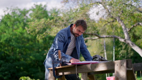 A mature man engineer with blueprints of a house outdoors.