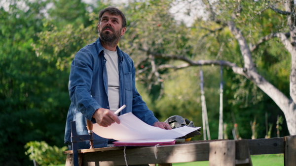 A mature man engineer with blueprints of a house outdoors.