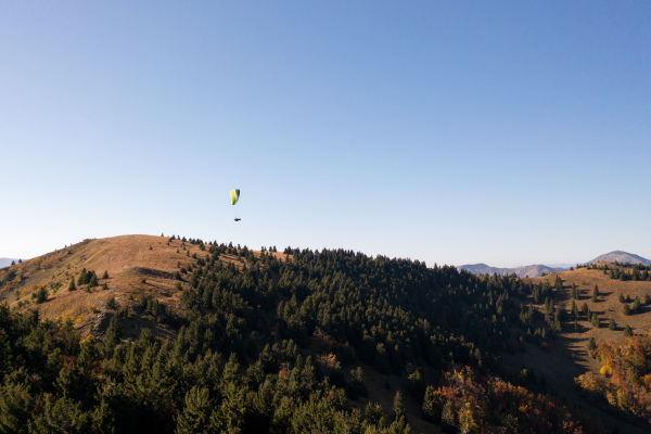 A paraglider flying in the blue sky with mountain in background.