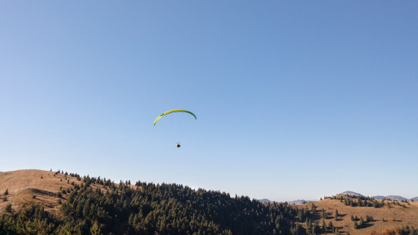 A paraglider flying in the blue sky with mountain in background.