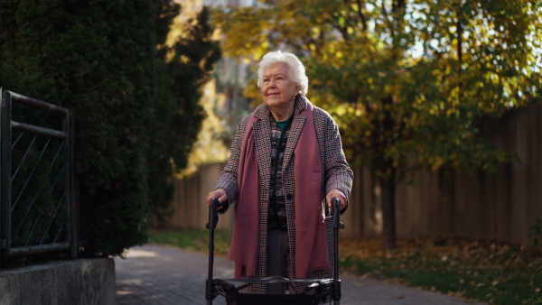 A happy senior woman on walk with walker in city in winter.