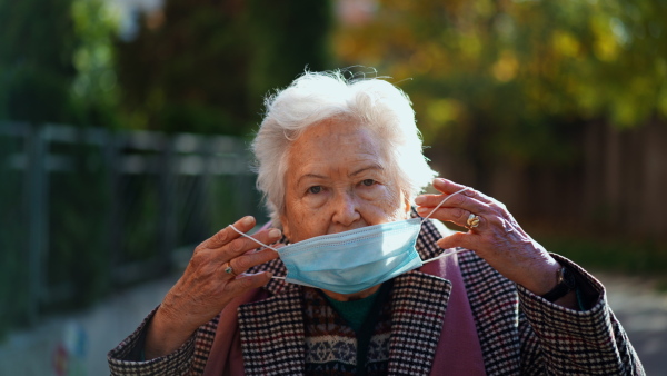 A senior woman putting on face mask outdoors in street.