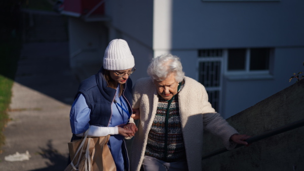 Caregiver helping senior woman to walk up stairs in town in winter.