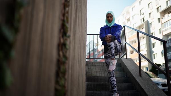 A low angle view of sporty young Muslim woman in hijab exercising outdoors in city.