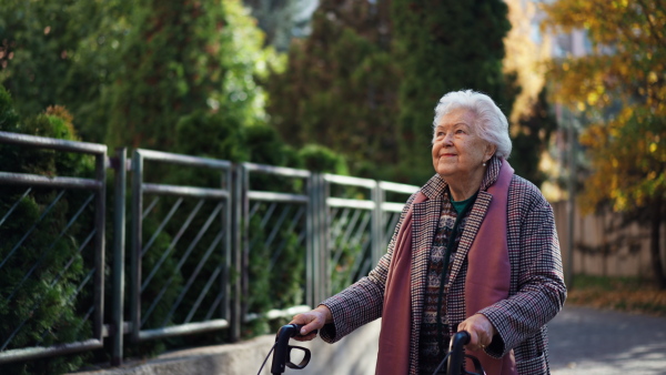 A happy senior woman on walk with walker in city in winter.