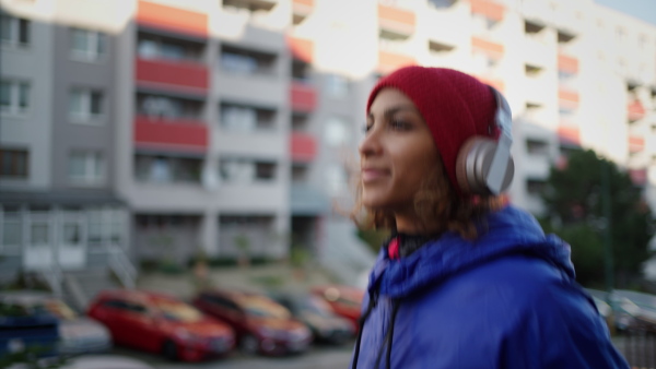 A sporty young multiracial woman with headphones running outdoors in city street.