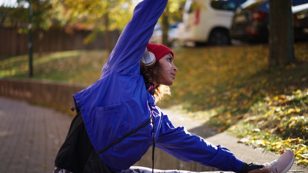 A sporty young multiracial woman with headphones doing stretching exercise outdoors in city street.