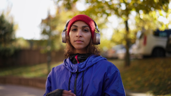 A sporty young multiracial woman with headphones outdoors in city street, looking at camera.