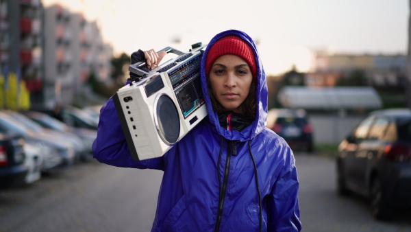 A young Muslim woman outdoors in the city, carrying a stereo radio and looking at camera.