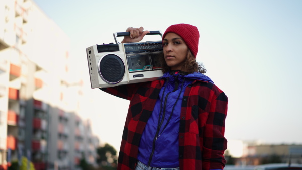 A young Muslim woman outdoors in the city, carrying a stereo radio and looking at camera.