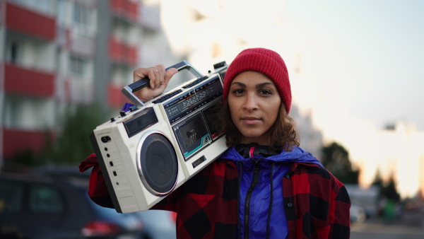 A young Muslim woman outdoors in the city, carrying a stereo radio and looking at camera.