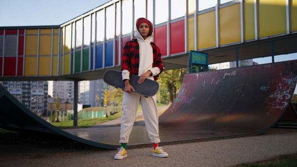 A young multiracial woman outdoors in the city, with skateboard looking at camera.