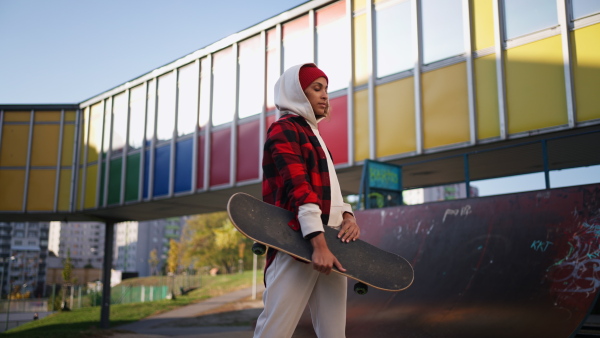 A young multiracial woman outdoors in the city, with skateboard looking at camera.