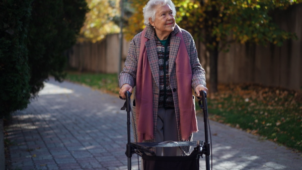 A happy senior woman on walk with walker in city in winter.