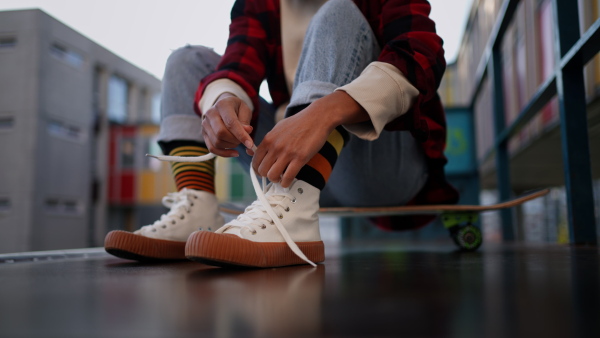 A close-up of modern urban girl tying sneakers in street.