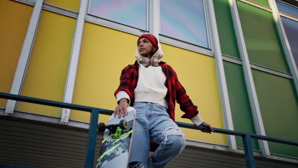 A young multiracial woman outdoors in the city, with skateboard looking at camera.