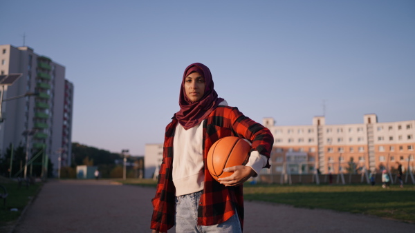 A low angle view of sporty young Muslim woman in hijab exercising outdoors in city, looking at camera.