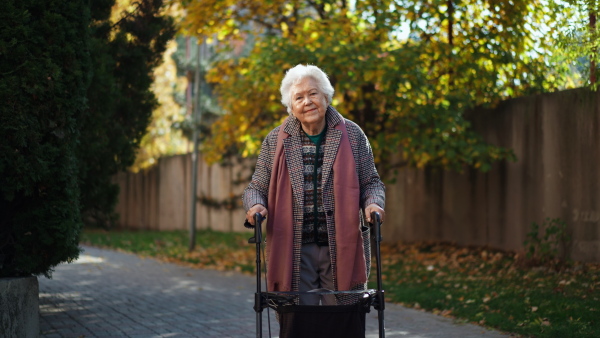 A happy senior woman on walk with walker in city in winter.