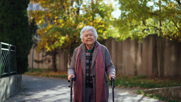 A happy senior woman on walk with walker in city in winter, looking at camera,