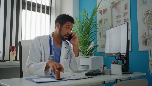 A young male doctor managing phone calls in his office, telemedicine concept.