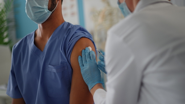 A close-up of doctor getting covid-19 vaccince from his colleague.