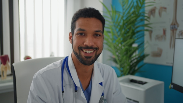 A happy young male doctor sitting at desk and looking at camera in his office.