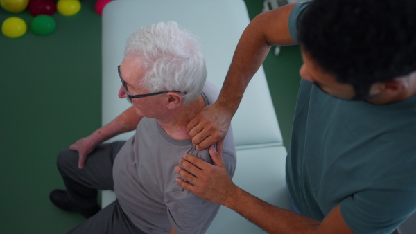 A high angle view of young physiotherapist massaging the shoulder of senior patient in a physic room