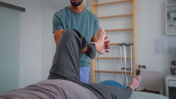 A close-up of physiotherapist exercising with senior patient's leg in a physic room.