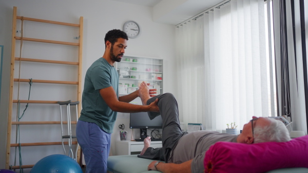 A physiotherapist exercising with senior patient's leg in a physic room.