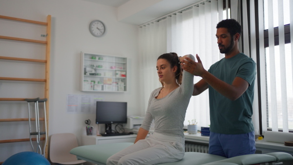 A young male physiotherapist exercising with young woman patient in a physic room