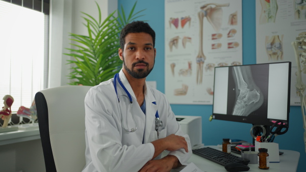 A young male doctor sitting at desk and looking at camera in his office.