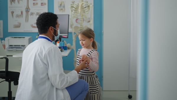 A zoung male doctor checking little girl's throat in his office.