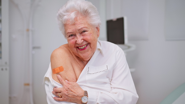 A happy senior woman showing bandage on arm after vaccination in doctor's office.