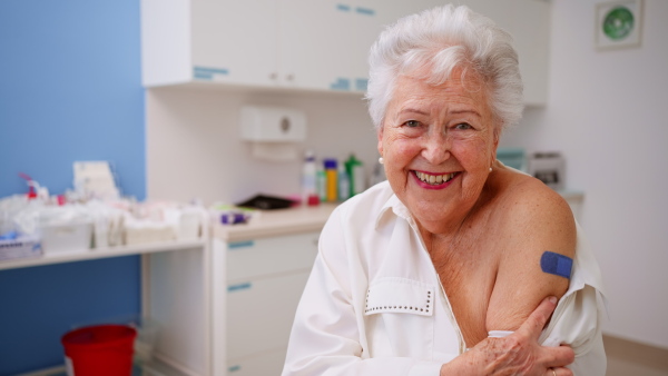 A happy senior woman showing bandage on arm after vaccination in doctor's office.