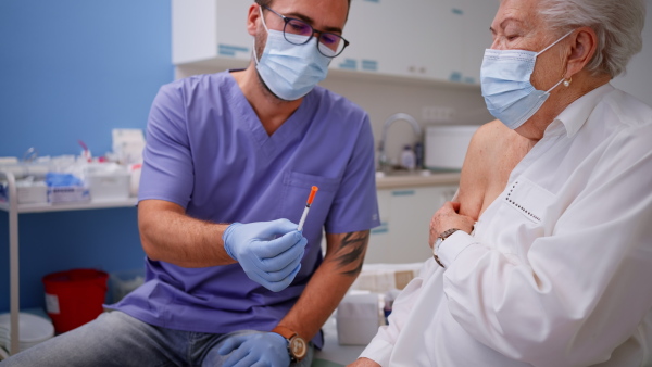 A doctor showing coronavirus vaccine to senior woman in his office.