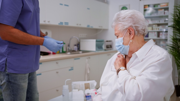 A doctor giving coronavirus vaccine to senior woman in his office.